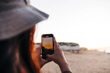 Frau fotografiert mit Smartphone am Strand bei Sonnenuntergang - ASGF01280