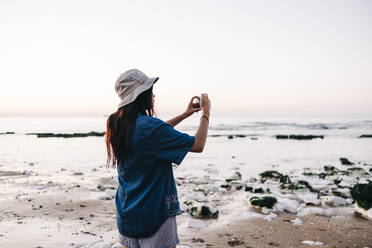 Frau mit Hut beim Fotografieren am Strand im Urlaub - ASGF01281