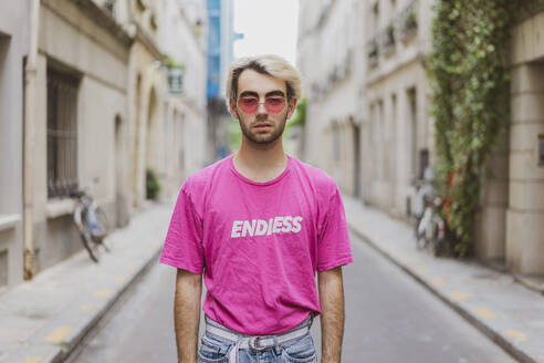 Young gay man in pink t-shirt standing on street - AFVF09046