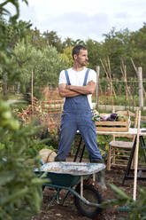 Male farmer looking away while standing with arms crossed at agricultural field - VEGF04952