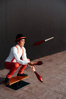 Full body of agile professional young male circus performer juggling clubs and balancing on board - ADSF29138