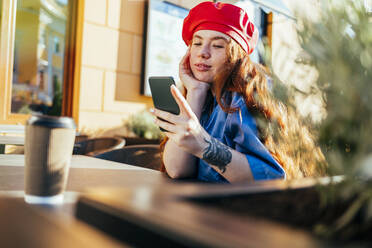 Junge Frau benutzt Mobiltelefon in einem Straßencafé - OYF00440