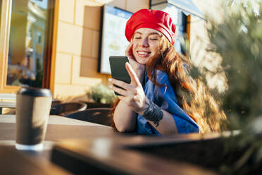 Smiling young woman using smart phone at sidewalk cafe - OYF00442