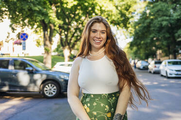 Smiling woman with long hair standing on road - OYF00469