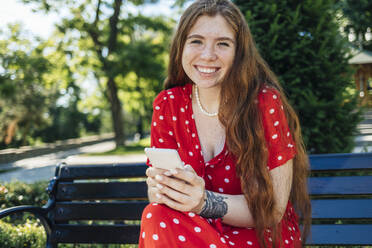 Frau hält Smartphone, während sie im Sommer im Park sitzt - OYF00483