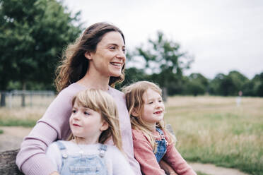 Smiling mother sitting with daughters at public park - ASGF01283