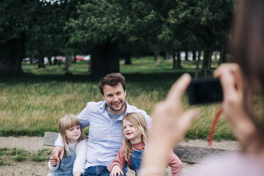 Woman photographing man and girls through camera at park - ASGF01289