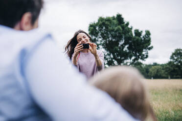 Lächelnde Frau fotografiert Familie durch Kamera im Park - ASGF01290