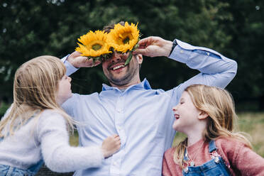 Fröhlicher Vater hält Sonnenblumen, während er mit seiner Tochter im Park spielt - ASGF01295
