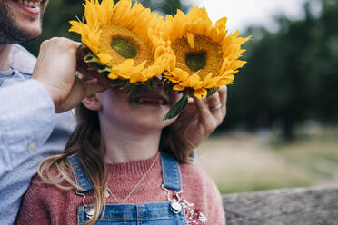 Mann bedeckt das Gesicht eines Mädchens im Park mit Sonnenblumen - ASGF01297