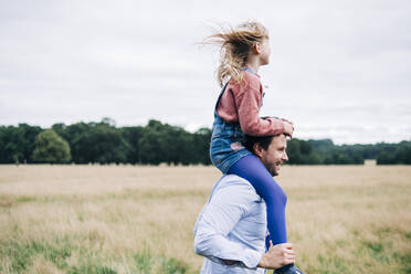 Happy father carrying daughter on shoulders at meadow - ASGF01305