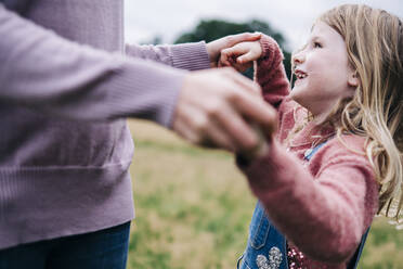 Smiling daughter holding hands of mother while playing outdoors - ASGF01310