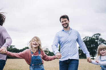 Man and woman holding hands of girls while running on meadow - ASGF01316