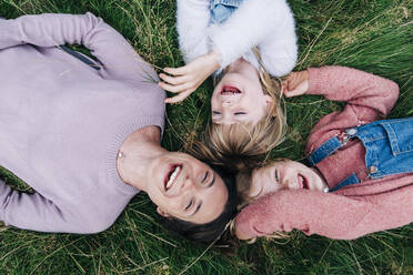 Cheerful mother and daughters lying on meadow - ASGF01344