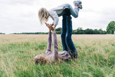 Mother playing with daughter while lying on meadow - ASGF01346