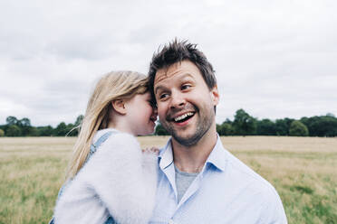 Daughter whispering in smiling father's ear at meadow - ASGF01353