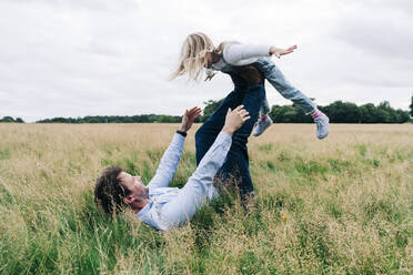 Vater balanciert Tochter beim Spielen auf der Wiese - ASGF01356