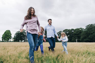 Smiling parents and daughters running together on meadow - ASGF01364