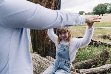 Daughter holding hand of father while sitting on fallen tree - ASGF01370