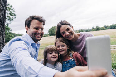 Lächelnder Vater, der ein Selfie mit seiner Familie über sein Smartphone im Park macht - ASGF01373