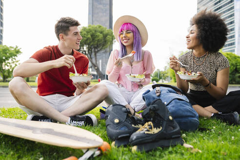 Glückliche junge Freunde essen Salat, während sie im Park sitzen - JCCMF03685