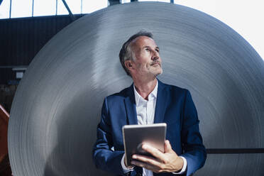 Nachdenklicher männlicher Geschäftsmann stehend mit digitalem Tablet in der Metallindustrie - GUSF06126