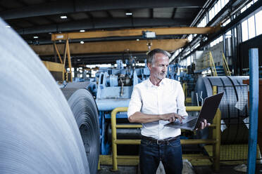 Senior businessman using laptop while standing in metal industry - GUSF06157