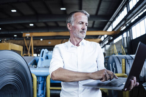 Geschäftsmann, der einen Laptop benutzt, während er in der Metallindustrie steht - GUSF06158