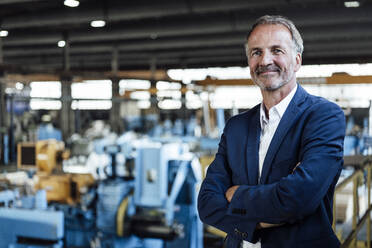 Confident businessman with arms crossed standing in steel mill - GUSF06228