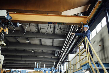 Männlicher Ingenieur, der auf einen Brückenkran zeigt, während er in einem Stahlwerk steht - GUSF06305