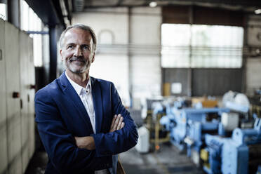 Male business professional with arms crossed standing at metal industry - GUSF06306