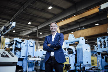 Smiling businessman with arms crossed standing at steel mill - GUSF06312