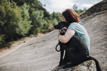 Mittlere erwachsene Frau, die ihren Hund auf einem Felsen umarmt - MRRF01409