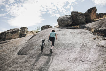 Mittlere erwachsene Frau und Hund laufen auf einer Felslandschaft - MRRF01410