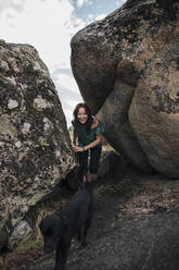 Smiling woman and dog walking amidst rocks - MRRF01411