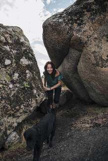 Lächelnde Frau und Hund beim Spaziergang inmitten von Felsen - MRRF01411