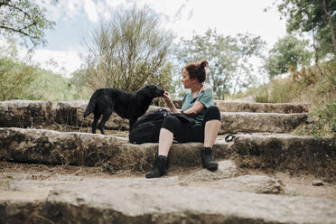 Mittlere erwachsene Frau, die ihren Hund im Wald füttert - MRRF01416