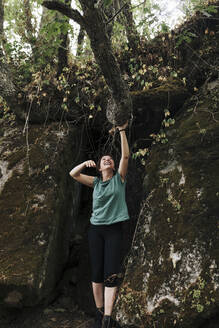 Lächelnde erwachsene Frau, die einen Ast im Wald hält, am Wochenende - MRRF01418