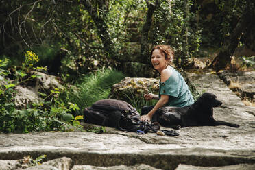 Glückliche mittelgroße erwachsene Frau mit Hund und Rucksack im Wald - MRRF01435