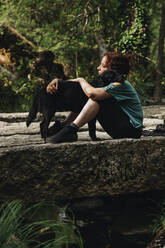 Mid adult female pet owner embracing dog in forest - MRRF01437