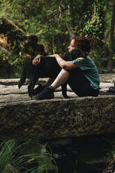 Mittlere erwachsene Tierhalterin umarmt Hund im Wald - MRRF01437