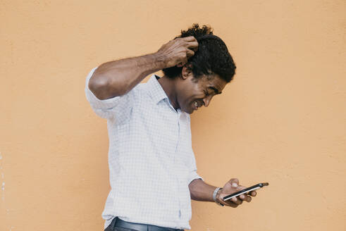 Frustrated man using smart phone in front of beige wall - DSIF00557
