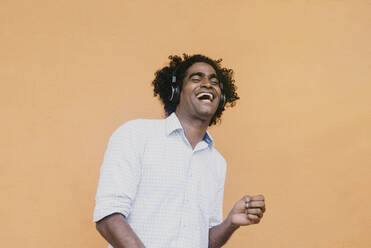 Mann lacht, während er über Kopfhörer vor einer Wand Musik hört - DSIF00562