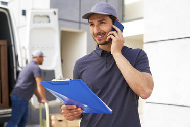 Smiling male delivery person looking away while talking on smart phone - ABIF01530