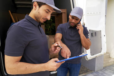 Delivery man talking on smart phone while explaining documents to colleague - ABIF01531