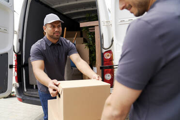 Zusteller sieht seinen Kollegen an, während er eine Kiste aus einem Umzugswagen auslädt - ABIF01544