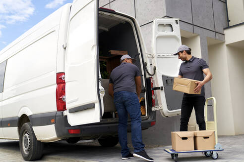 Delivery men loading cardboard box in van - ABIF01548