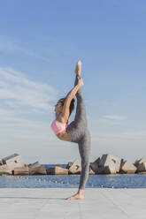 Woman standing on one leg while practicing acroyoga on boardwalk - AFVF09106