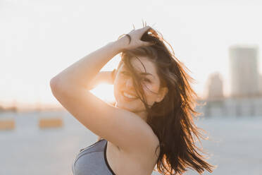 Lächelnde Frau mit Hand im Haar bei Sonnenuntergang - AFVF09117