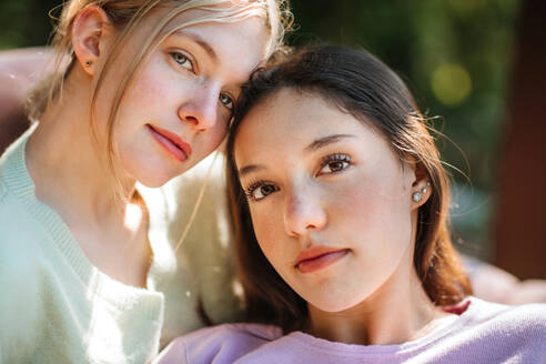 Tender teen sisters looking at camera on sunny summer day in green garden - ADSF29240